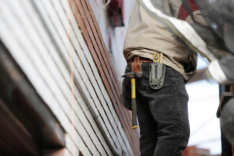 Un artisan sur une façade, marteau et outils à la ceinture